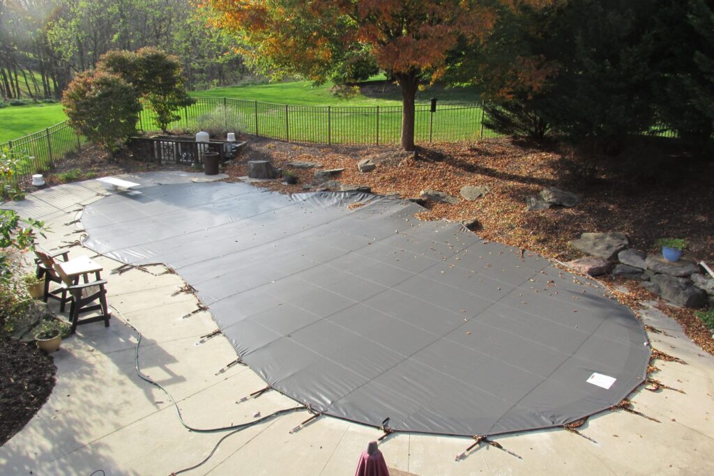 Rectangular pool secured with a gray mesh cover and stone landscaping.
