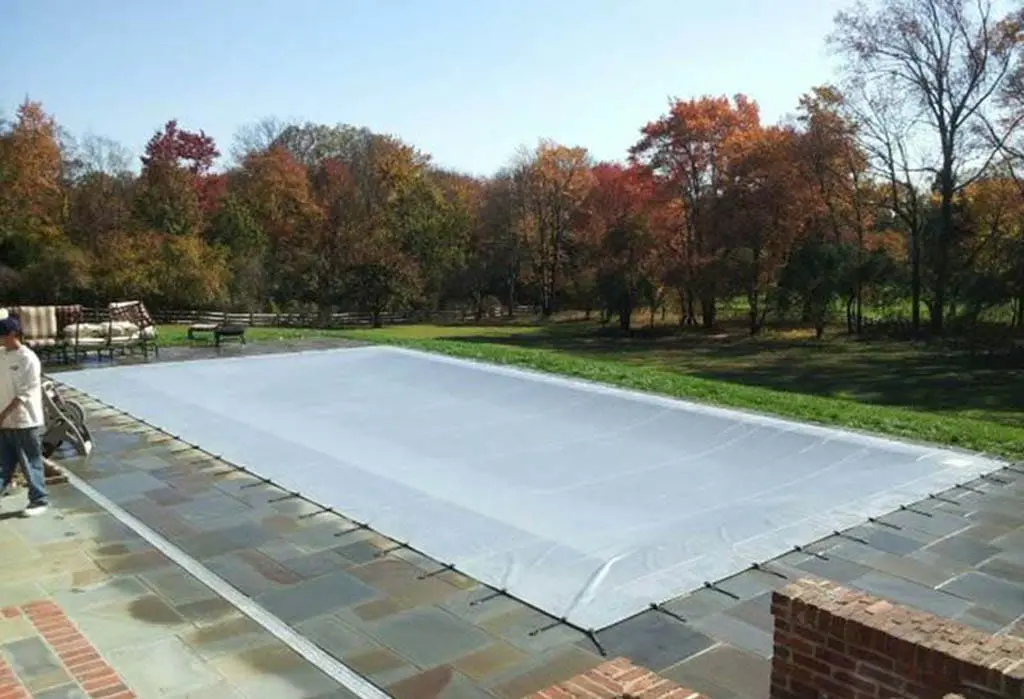 Light gray safety pool cover installed on outdoor residential pool