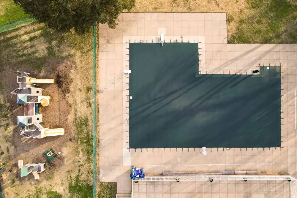 Dark gray rectangular safety pool cover installed on backyard swimming pool