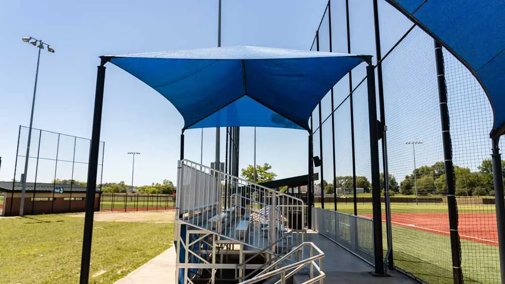 Blue fabric canopy over bleacher seating near glass building.